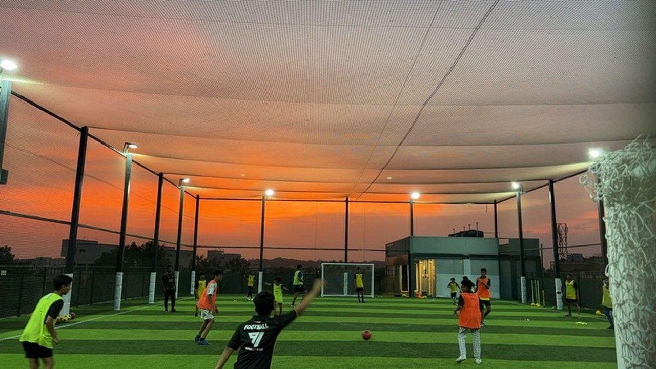 Players training on a floodlit rooftop football turf at dusk, 91 Sporting Co.